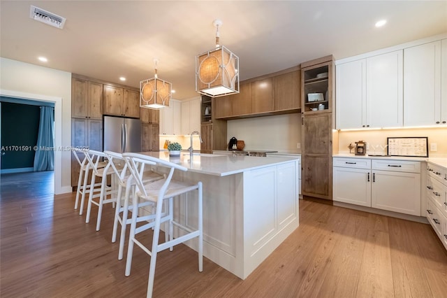 kitchen with a kitchen island with sink, decorative light fixtures, stainless steel fridge, and white cabinets