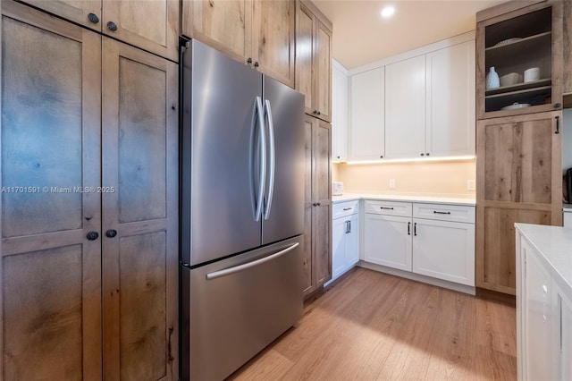 kitchen with light wood-type flooring, white cabinets, and stainless steel refrigerator