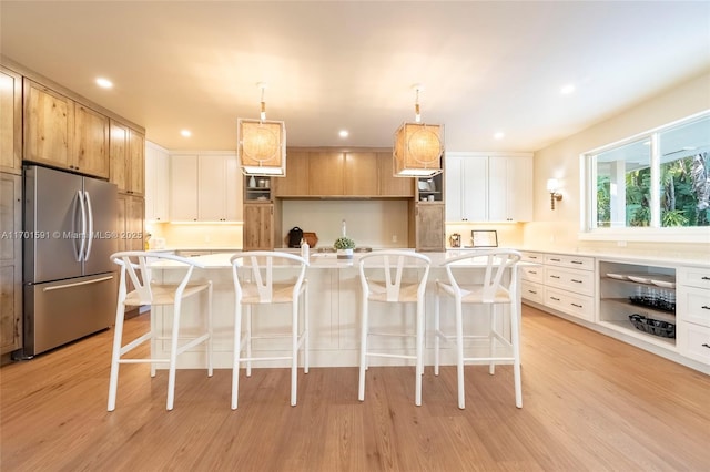 kitchen featuring stainless steel refrigerator, an island with sink, white cabinetry, a breakfast bar area, and hanging light fixtures