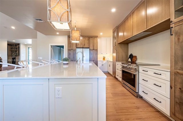 kitchen with a large island with sink, white cabinets, sink, light wood-type flooring, and stainless steel appliances