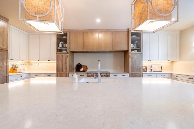 kitchen featuring light stone counters, pendant lighting, sink, and white cabinets