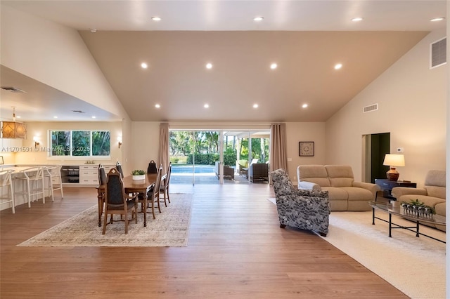 dining space with high vaulted ceiling and light hardwood / wood-style flooring