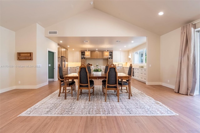 dining room with high vaulted ceiling and light hardwood / wood-style floors