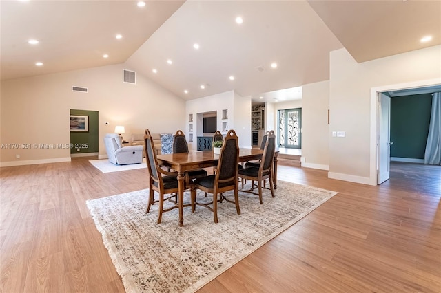 dining space with high vaulted ceiling and light hardwood / wood-style floors