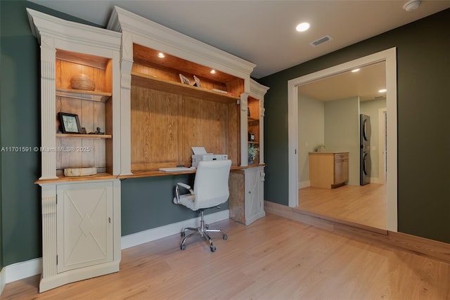 office area with light wood-type flooring, built in desk, and stacked washer / dryer