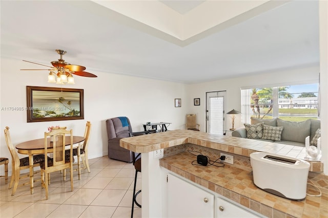 kitchen with kitchen peninsula, ceiling fan, light tile patterned floors, white cabinetry, and a breakfast bar area