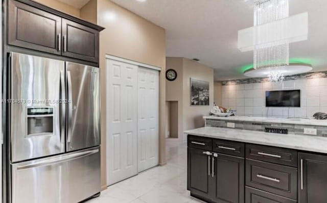 kitchen featuring decorative backsplash, light stone counters, dark brown cabinetry, and stainless steel refrigerator with ice dispenser