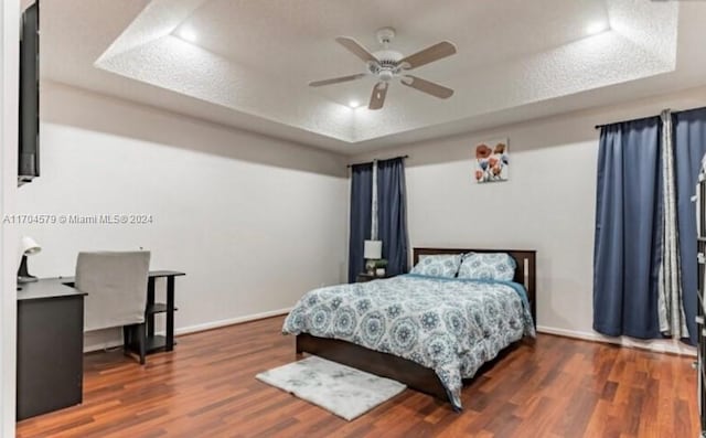 bedroom with a raised ceiling, ceiling fan, dark hardwood / wood-style flooring, and a textured ceiling