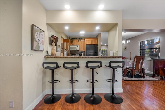 kitchen with black fridge, wood-type flooring, a kitchen bar, kitchen peninsula, and a chandelier