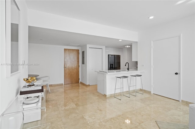 kitchen with white cabinetry, sink, stainless steel fridge with ice dispenser, kitchen peninsula, and a kitchen bar