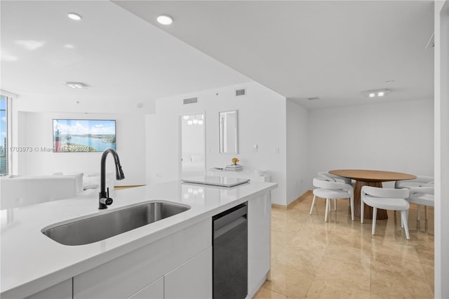 kitchen featuring dishwashing machine, sink, and white cabinets