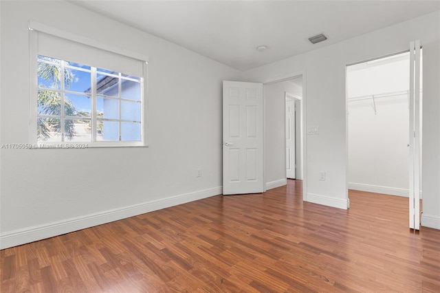 unfurnished bedroom with a walk in closet, a closet, and hardwood / wood-style flooring