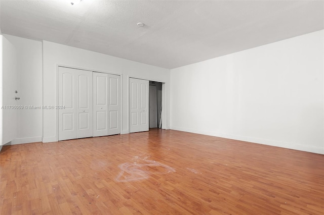 unfurnished bedroom with a textured ceiling, light hardwood / wood-style flooring, and multiple closets