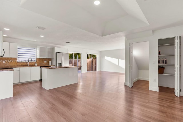 kitchen featuring sink, light hardwood / wood-style flooring, stainless steel fridge, a kitchen island, and white cabinetry