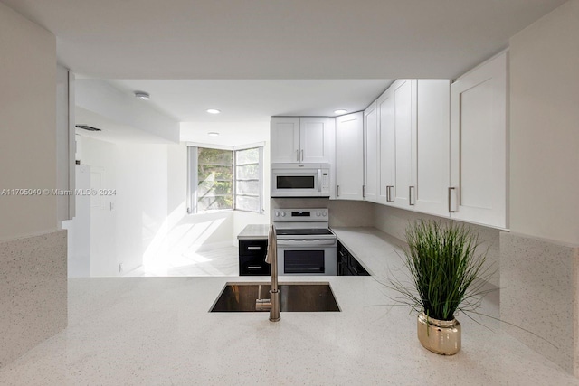 kitchen featuring white cabinets, white appliances, light stone counters, and sink