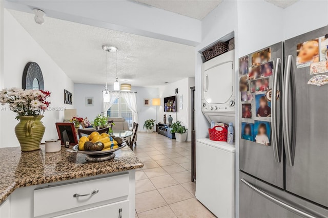 kitchen with dark stone counters, stainless steel fridge, stacked washing maching and dryer, light tile patterned flooring, and white cabinetry