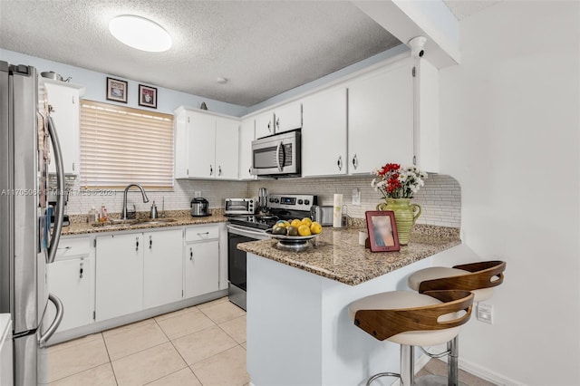 kitchen featuring kitchen peninsula, appliances with stainless steel finishes, dark stone counters, sink, and white cabinets