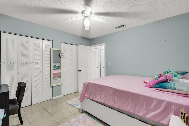 tiled bedroom with ceiling fan, a textured ceiling, and multiple closets