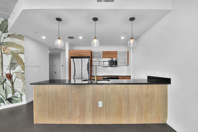 kitchen featuring decorative backsplash, kitchen peninsula, stainless steel appliances, dark tile patterned floors, and sink