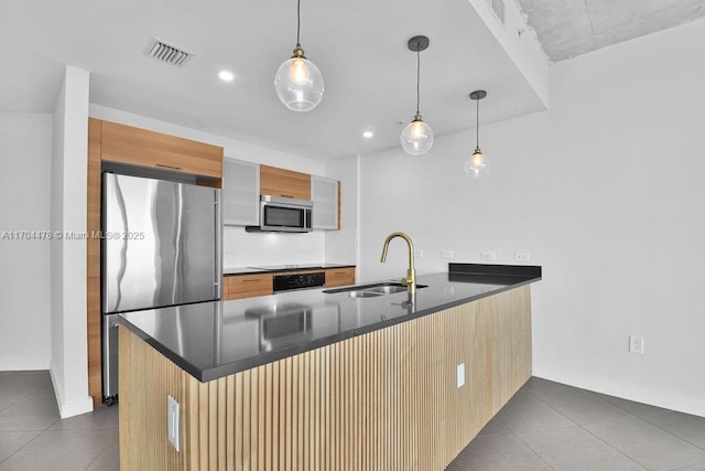 kitchen featuring kitchen peninsula, appliances with stainless steel finishes, tasteful backsplash, sink, and decorative light fixtures