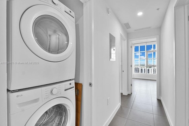 clothes washing area featuring light tile patterned floors, electric panel, and stacked washing maching and dryer