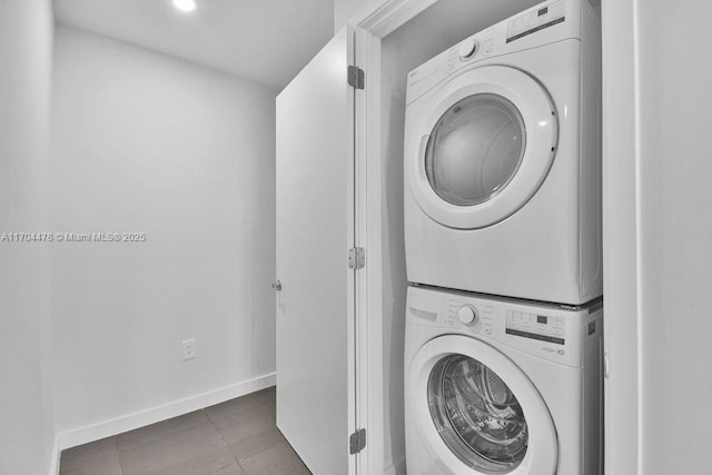 washroom featuring stacked washer / drying machine and dark tile patterned floors