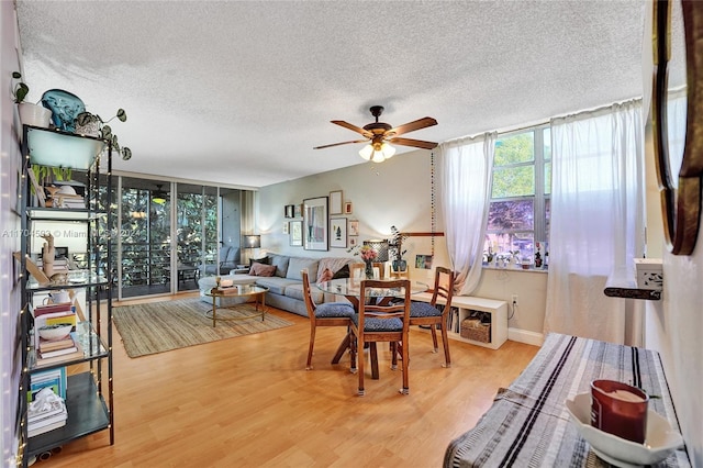 living room with ceiling fan, wood-type flooring, a textured ceiling, and a wall of windows