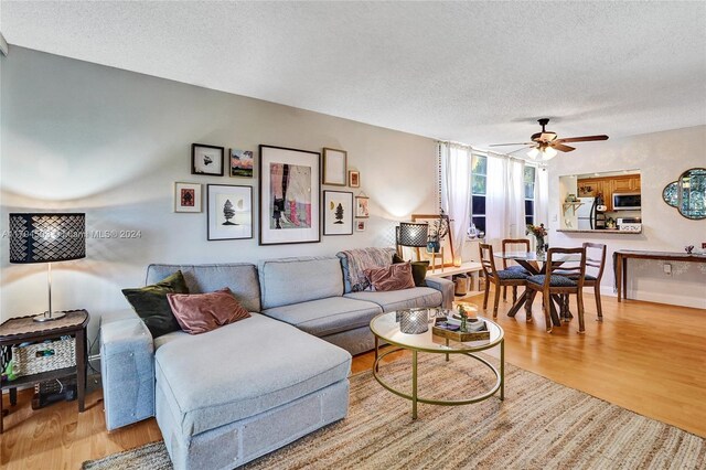 living room featuring ceiling fan, a textured ceiling, and light wood-type flooring