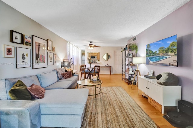 living room featuring a textured ceiling, light wood-type flooring, and ceiling fan