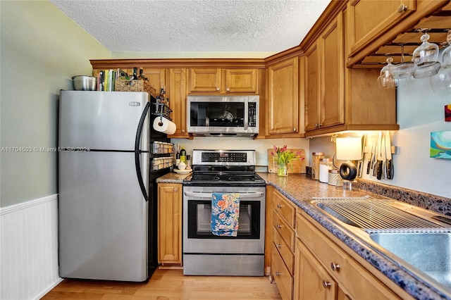 kitchen with appliances with stainless steel finishes, a textured ceiling, light hardwood / wood-style floors, and dark stone countertops