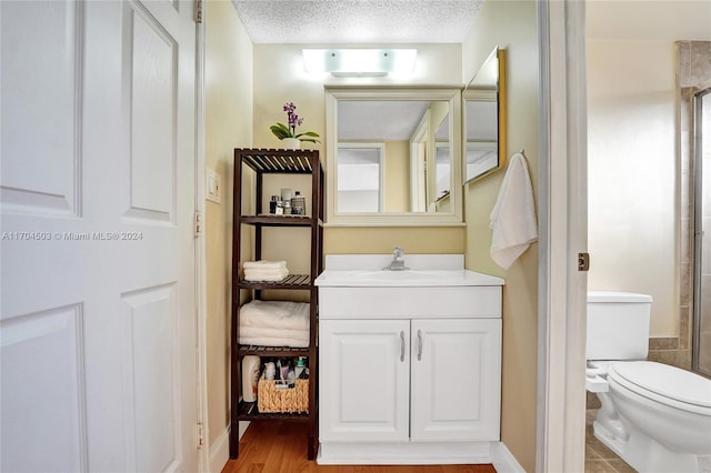 bathroom featuring wood-type flooring, an enclosed shower, a textured ceiling, toilet, and vanity