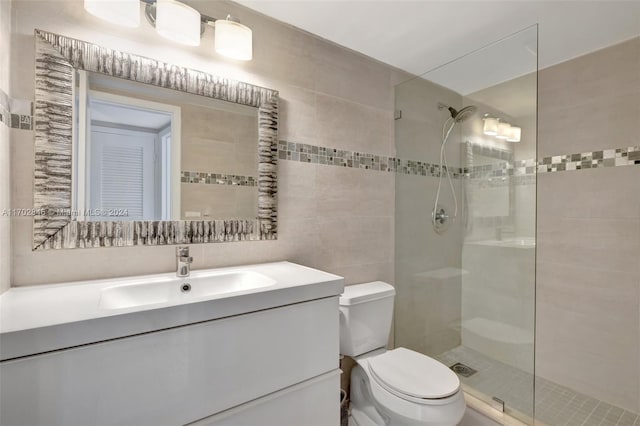 bathroom with a tile shower, vanity, toilet, and tile walls