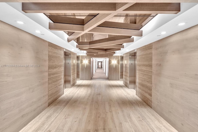 corridor with wood walls, beam ceiling, light hardwood / wood-style floors, and elevator