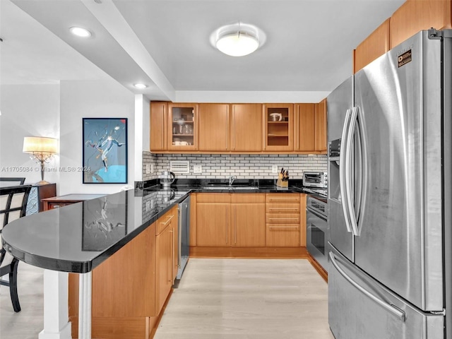 kitchen featuring appliances with stainless steel finishes, light wood-type flooring, backsplash, sink, and dark stone countertops