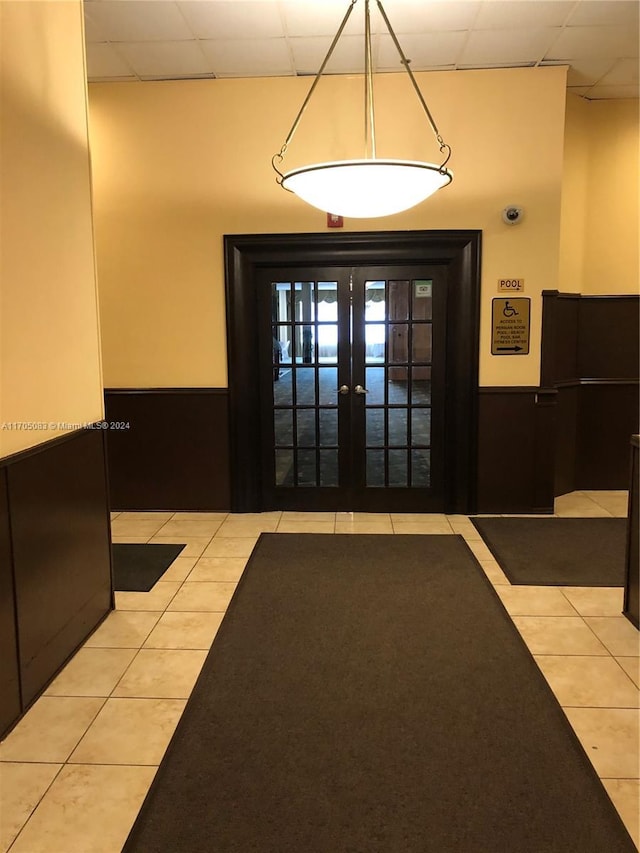 doorway with french doors, light tile patterned floors, and a drop ceiling