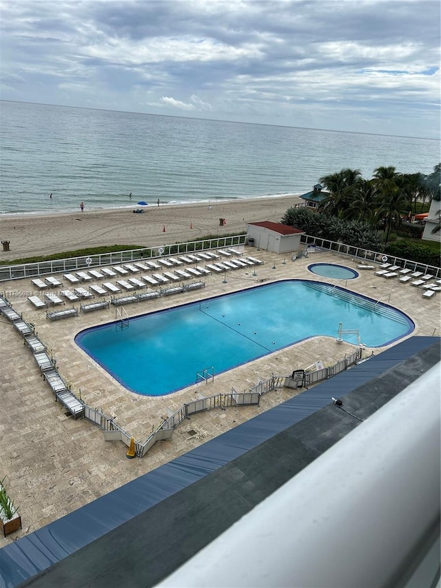 view of pool with a water view, a community hot tub, a patio, and a view of the beach