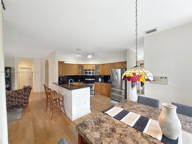 kitchen with kitchen peninsula, a kitchen bar, backsplash, stainless steel appliances, and light hardwood / wood-style floors