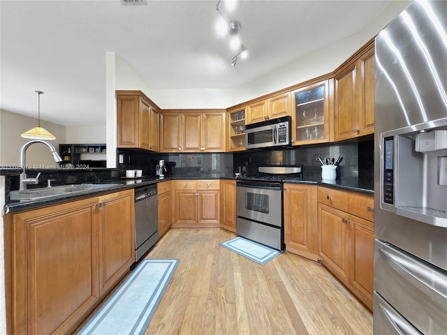 kitchen featuring decorative backsplash, appliances with stainless steel finishes, dark stone counters, sink, and light hardwood / wood-style flooring