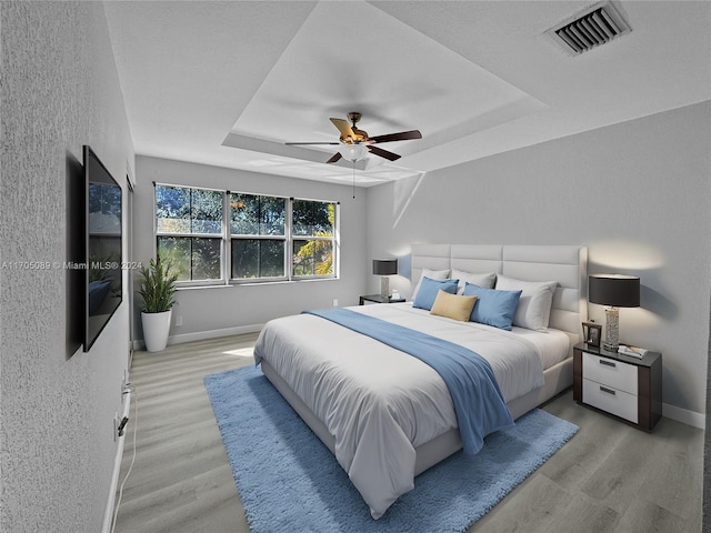 bedroom with a tray ceiling, ceiling fan, and light wood-type flooring