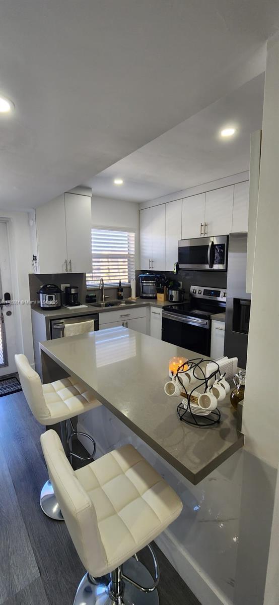 kitchen with a kitchen breakfast bar, white cabinetry, sink, and appliances with stainless steel finishes