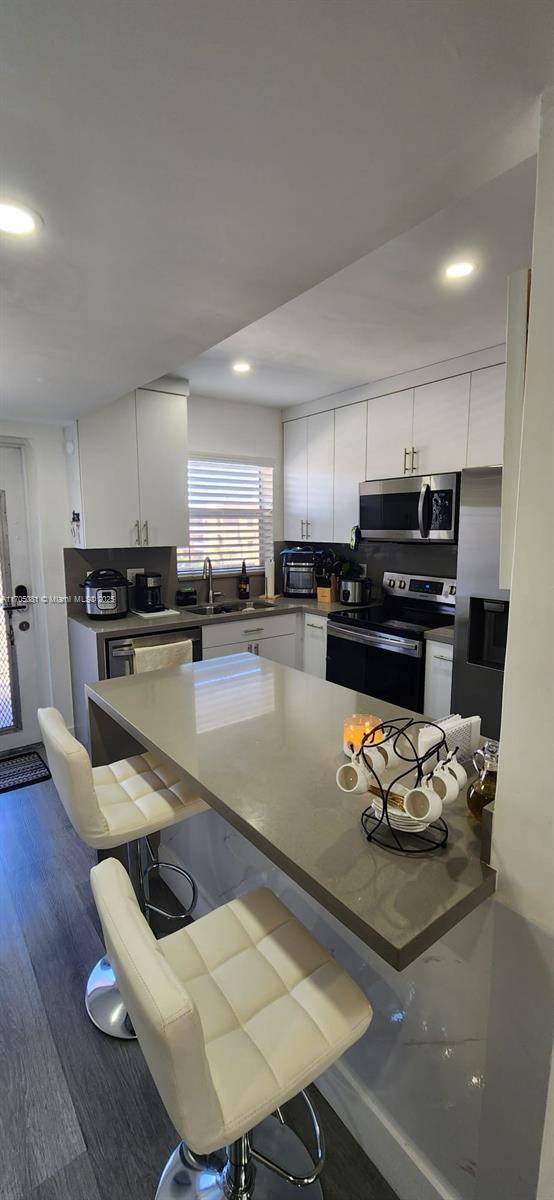 kitchen featuring sink, decorative backsplash, appliances with stainless steel finishes, white cabinetry, and a breakfast bar area