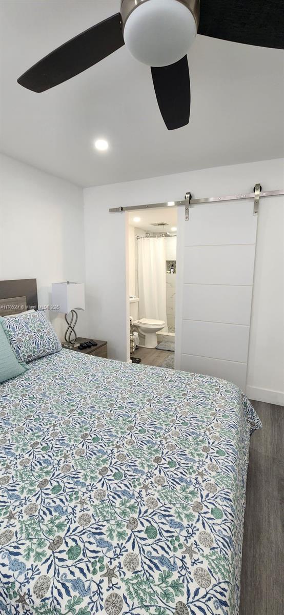 bedroom featuring ensuite bathroom, a barn door, dark hardwood / wood-style flooring, and ceiling fan