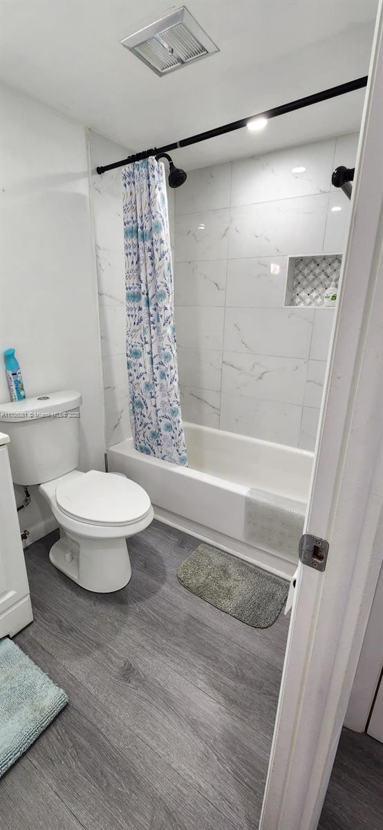 bathroom with hardwood / wood-style floors, shower / bathtub combination with curtain, and toilet