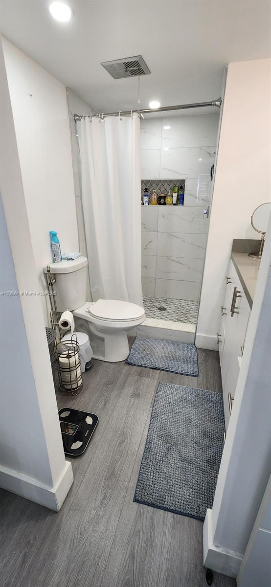 bathroom with a stall shower, visible vents, toilet, and wood finished floors