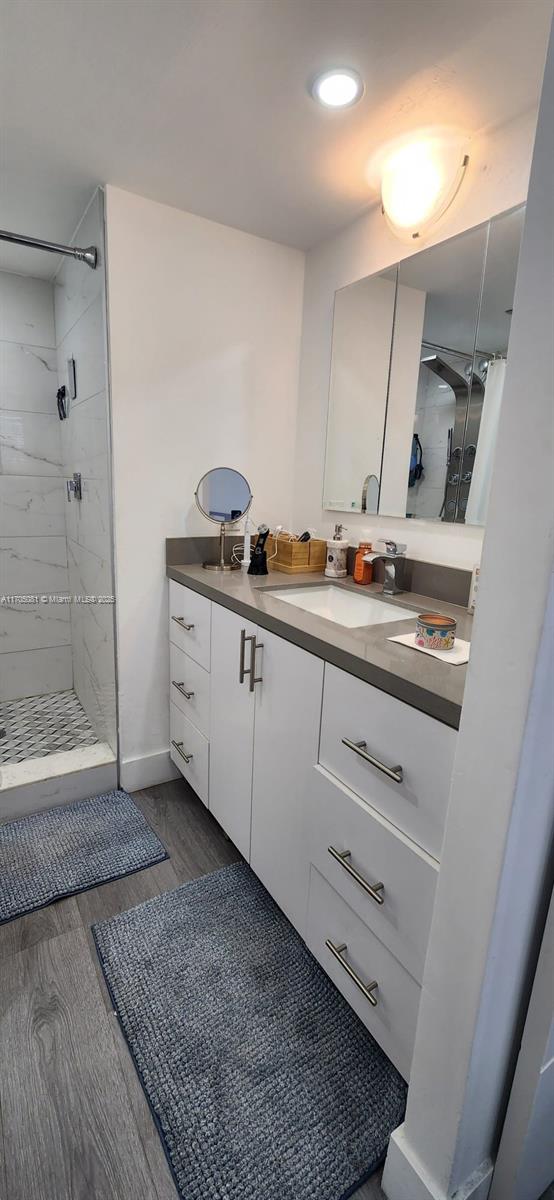 full bathroom with recessed lighting, tiled shower, vanity, and wood finished floors