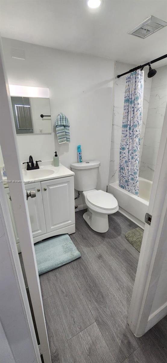 full bathroom with shower / bath combination with curtain, vanity, wood-type flooring, and toilet