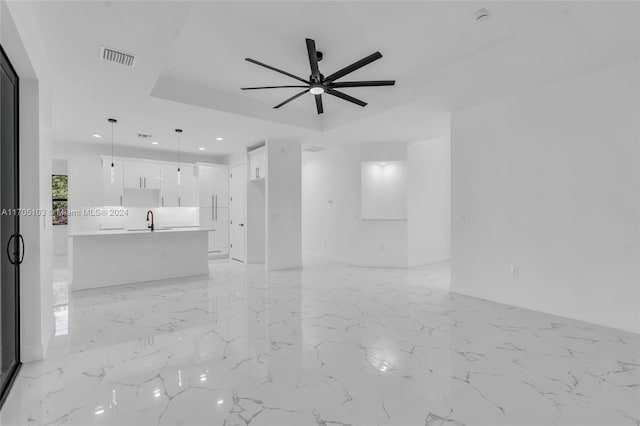 unfurnished living room featuring a tray ceiling, ceiling fan, and sink