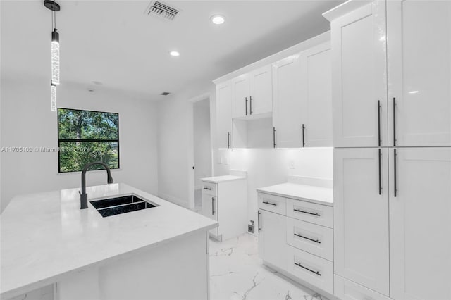 kitchen featuring sink, white cabinets, an island with sink, and decorative light fixtures