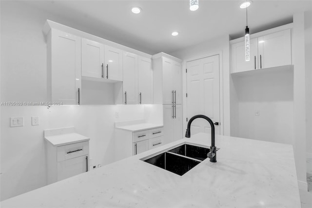 kitchen featuring light stone countertops, sink, white cabinets, and hanging light fixtures