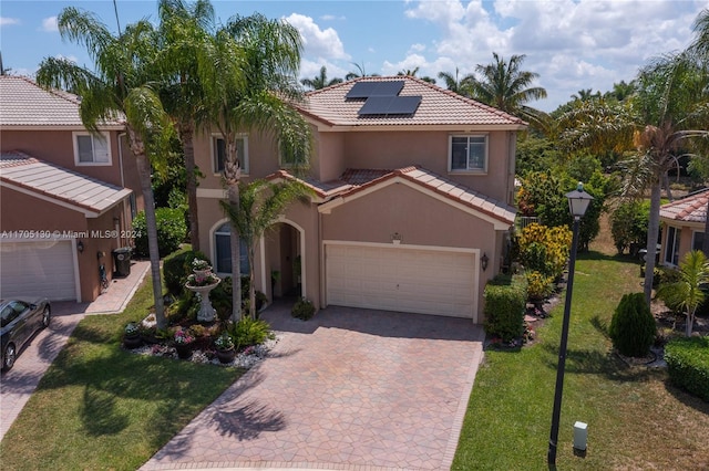 mediterranean / spanish home featuring solar panels, a garage, and a front lawn